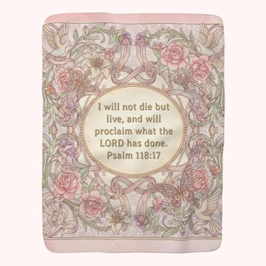 Puede incluir: Una manta rosa claro con un diseño floral con rosas, mariposas y palomas. El centro tiene un óvalo con el texto "I will not die but live, and will proclaim what the LORD has done. Psalm 118:17."