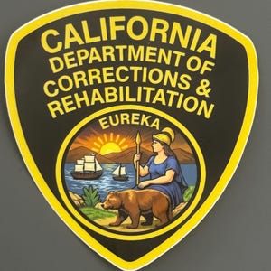 May include: A shield-shaped patch featuring the text CALIFORNIA DEPARTMENT OF CORRECTIONS & REHABILITATION in yellow on a black background. The center displays the California state seal with a bear, a figure with a spear, and a ship.