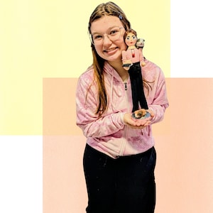 May include: A custom nutcracker figurine featuring a person with brown hair wearing a pink top and black pants, holding a small black book. A small white and black animal sits on the shoulder, and a brown and white animal sits on the base.