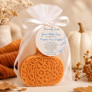 May include: An orange pumpkin-shaped goat milk soap with a leopard print texture, packaged in a white organza drawstring bag with a white ribbon. A circular tag reads Heavenly Scents Goat Milk Soap Scented with Pumpkin Pecan Waffles, 4 oz.