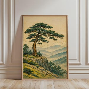 Könnte beinhalten: Gerahmter Druck eines japanischen Landschaftsbildes. Es zeigt einen großen Baum mit grünen Blättern auf einer Klippe mit einer nebligen Bergkette im Hintergrund. Das Kunstwerk hat eine Vintage-Ästhetik.