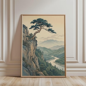 Könnte beinhalten: Gerahmter Kunstdruck mit einer ruhigen Berglandschaft. Ein Baum wächst von einer Klippe, die einen Fluss überblickt, der sich durch ein Tal schlängelt. Das Kunstwerk verwendet gedämpfte Grün-, Blau- und Beigetöne und schafft eine beruhigende Ästhetik.