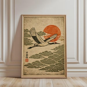 Könnte beinhalten: Ein gerahmter Druck mit einer japanisch anmutenden Illustration eines fliegenden Kranichs. Das Kunstwerk zeigt eine rote Sonne, stilisierte Wolken und einen Kranich mit schwarz-weißem Gefieder. Der Druck hat japanischen Text und ein rotes Siegel.