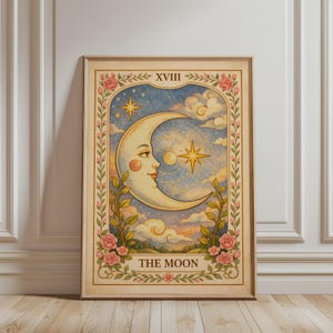 Könnte beinhalten: Gerahmter Tarotkarten-Druck mit einem Mondgesicht, Sternen und Wolken. Die Karte trägt die Aufschrift "THE MOON" und hat einen floralen Rahmen mit rosa Rosen. Der Hintergrund ist ein hellblauer Himmel.