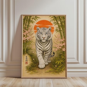 Könnte beinhalten: Gerahmter Kunstdruck mit einem weißen Tiger, der auf den Betrachter zugeht. Der Tiger ist vor einem Hintergrund aus Bambus, Kirschblüten und einer aufgehenden orangefarbenen Sonne platziert. Das Kunstwerk hat eine Vintage-Ästhetik im asiatischen Stil.