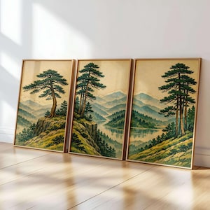 May include: Set of three framed landscape prints. Each print features a serene mountain scene with pine trees and a lake. The artwork has a vintage aesthetic with muted green, blue, and beige tones, and is framed in a light wood.
