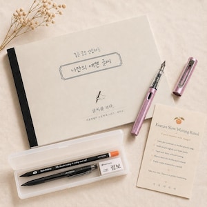 Op de afbeelding: Een briefpapierset met een lichtroze vulpen, een notitieboek met Koreaanse tekst en een transparante etui met pennen en een gum. Er is ook een kleine kaart met Koreaanse tekst. Ontworpen voor kalligrafie en slow writing.