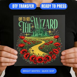 Könnte beinhalten: Ein DTF-Transfer mit einer farbenfrohen Illustration aus Der Zauberer von Oz. Das Design zeigt eine gelbe Ziegelstraße, ein grünes Schloss und rote Mohnblumen. Der Text "OFF TO SEE THE WIZARD" ist in Grün und Weiß dargestellt.