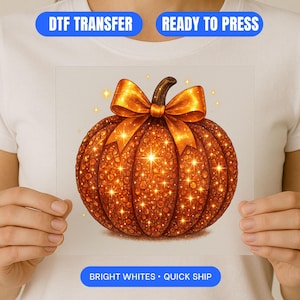 Peut inclure: Un transfert DTF avec une citrouille orange étincelante ornée d'un nœud doré. Le motif de la citrouille a une surface texturée et est prêt à être pressé. Le texte "DTF TRANSFER", "READY TO PRESS" et "BRIGHT WHITES • QUICK SHIP" est inclus.