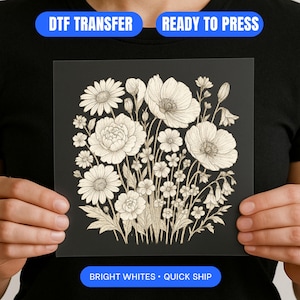 May include: A black square DTF transfer with a detailed white floral design. The design includes various flowers and foliage. The text "DTF TRANSFER", "READY TO PRESS", "BRIGHT WHITES", and "QUICK SHIP" are displayed on the transfer.