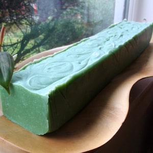 May include: A large, green bar of soap with a swirling pattern. The soap is sitting on a wooden surface.