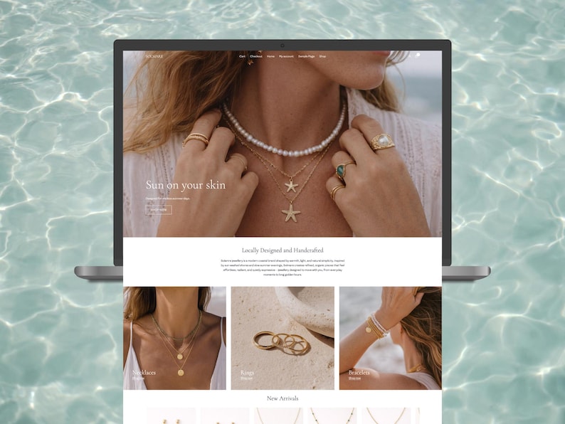 Op de afbeelding: Een laptop toont een sieradenwebsite met de tekst "Sun on your skin". De website toont kettingen, ringen en armbanden. Het model op de afbeelding draagt een parelketting, gouden kettingen en ringen. De achtergrond is een wateroppervlak.