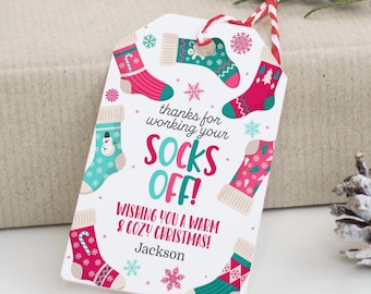May include: A white gift tag with a colorful Christmas sock design. The tag says "Thanks for working your socks off! Wishing you a warm & cozy Christmas!" with the name "Jackson" at the bottom.