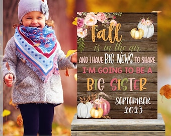 May include: A printable sign announcing a new baby with a fall theme. The sign has a wooden background with a floral design and pumpkins. The text reads "Fall is in the air and I have big news to share. I'm going to be a big sister. September 2023."