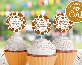 May include: Three brown and white cupcake toppers featuring the text "Carter's First Rodeo" and a cowboy hat design. The toppers are placed on top of cupcakes with white icing and brown sprinkles. A brown and gold personalised tag with the text "Personalize with Coril" is in the top right corner of the image.