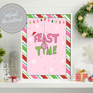 May include: A pink and green printable sign with the text "Feast Time" in white letters. The sign has a red and white striped border and a Christmas bauble hanging from the top.