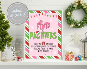 以下が含まれることがあります： 「Find the Pacifiers」のテキストが入った、額入りのピンクと白のクリスマスをテーマにしたサイン。サインには赤と緑のストライプのボーダーがあり、クリスマスライトと雪の結晶で飾られています。サインは、クリスマスの装飾が施された白い棚にあります。