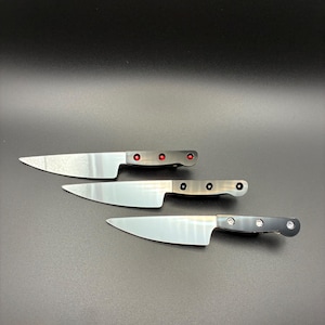 May include: Three stainless steel kitchen knives with silver blades and dark gray handles. The handles have red or black rivets. The knives are arranged diagonally against a dark background.
