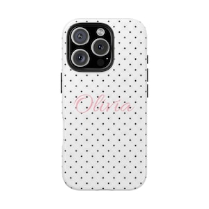 May include: White phone case with a black polka dot pattern. The case features a pink script font that spells out the name "Olivia". The phone case has a camera cutout and black side buttons.