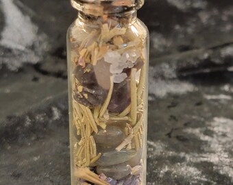 May include: A clear glass bottle with a cork stopper, filled with a variety of dried herbs, crystals, and stones. The contents include purple amethyst, green rosemary, and black stones. The bottle is cylindrical and appears to be about 4 inches tall.