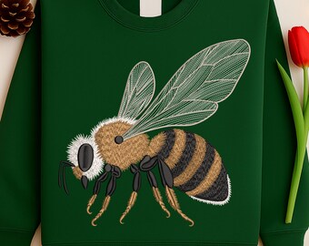 May include: A dark green sweatshirt featuring a detailed embroidered bee. The bee has a brown body with black and tan stripes, white accents, and transparent wings. The sweatshirt is a solid color, with a simple crew neck.