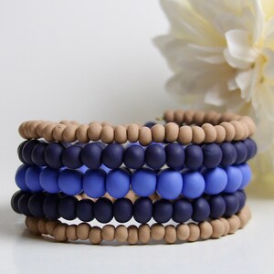 May include: A stack of five bracelets made of brown, dark blue, and light blue beads. The bracelets are arranged in a graduated pattern, with the brown beads at the top and the light blue beads at the bottom.