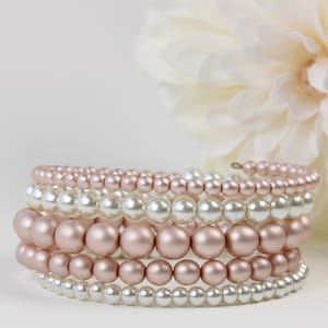 May include: A stack of pearl bracelets in white and rose gold tones. The bracelets are made of faux pearls and are arranged in a graduated size, with the largest pearls at the bottom and the smallest pearls at the top.