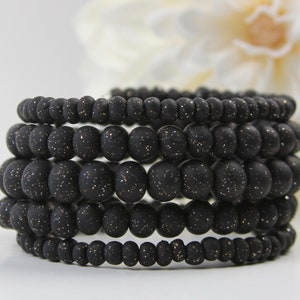 May include: A stack of six black bracelets made of small, round beads with a glittery finish.