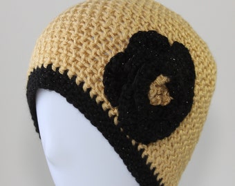 May include: A crocheted beanie hat in a light beige color with a black crocheted flower on the side.
