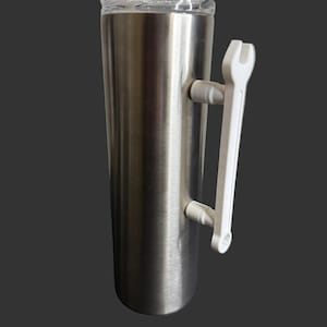 May include: A stainless steel tumbler with a clear lid and a white wrench-shaped handle. The tumbler has a cylindrical shape and a brushed metal finish. The handle is attached to the side of the tumbler.