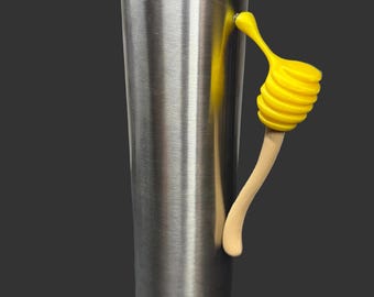 May include: A stainless steel tumbler with a clear lid and a yellow honey dipper handle. The handle is made of a wooden stick and a yellow spiral-shaped dipper. The tumbler is cylindrical and has a brushed metal finish.