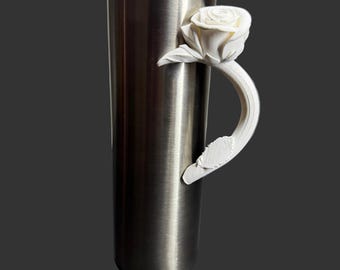 May include: A stainless steel tumbler with a clear lid and a white rose handle. The rose handle is 3D-printed and adds a decorative touch to the insulated drinkware. The tumbler is designed to keep beverages cold or hot.