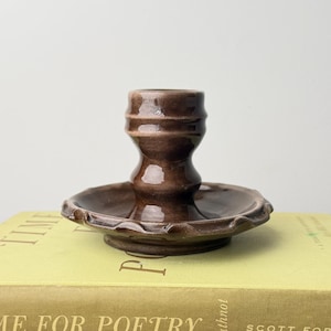 May include: A brown glazed ceramic candle holder with a wide, scalloped base and a central cylindrical socket, resting on two stacked books titled Time for Poetry by Arbuthnot and Printmaking with Monotype by Chilton.