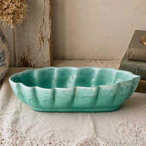 May include: An oval ceramic bowl with a scalloped edge and a glossy turquoise glaze. The interior and exterior feature a crackled texture, with a lighter, creamy white drip effect along the upper rim of the vessel, creating a distinct contrast.