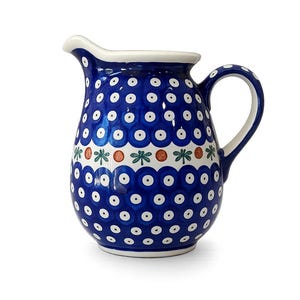 May include: A ceramic pitcher featuring a deep blue glaze with a repeating pattern of white dots. A central horizontal band displays alternating green floral motifs and orange circular accents. The pitcher has a curved handle and a pouring spout.