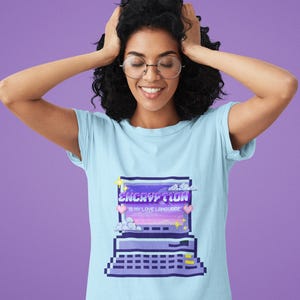 May include: Light blue t-shirt featuring a pixelated computer design with the words "ENCRYPTION IS MY LOVE LANGUAGE" in white and purple. The design includes stars, clouds, and hearts. The shirt is made of a soft material.