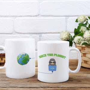 Puede incluir: Dos tazas de cerámica blanca. Una taza presenta un gráfico 3D de la Tierra. La otra taza tiene el texto "HACK THE PLANET" y un gráfico de una figura encapuchada con gafas de sol y un símbolo de código. Las tazas están sobre una superficie de madera.