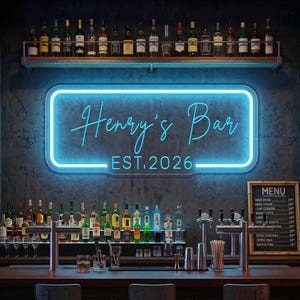 Op de afbeelding: Een rechthoekig neonbord met een heldere blauwe gloed met de tekst Henry's Bar EST. 2026 in een script- en schreefloos lettertype. Het bord is gemonteerd op een donkere getextureerde muur boven een houten bar met flessen en een menubord.