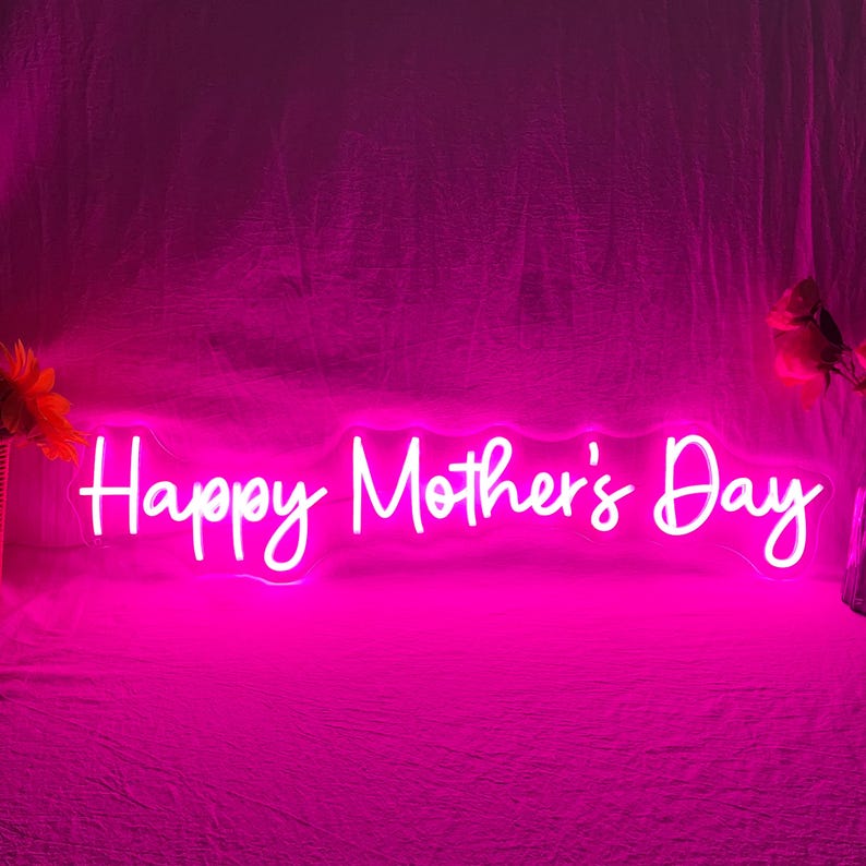 May include: A bright pink neon sign that reads "Happy Mother's Day" in a cursive font. The sign is illuminated against a pink background, creating a vibrant and celebratory atmosphere. The image is perfect for Mother's Day.