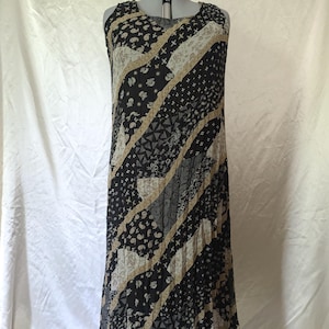 May include: A sleeveless floor-length dress featuring a diagonal patchwork pattern in black, white, and tan. The garment displays various intricate geometric and floral prints arranged in alternating stripes across the entire length of the fabric.