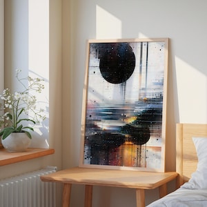 Może przedstawiać: Abstrakcyjny wydruk artystyczny w jasnej drewnianej ramie. Grafika przedstawia dwa duże czarne koła z pionowymi liniami i rozpryskami na białym i kolorowym tle. Wydruk jest eksponowany na drewnianym stole w pobliżu okna.