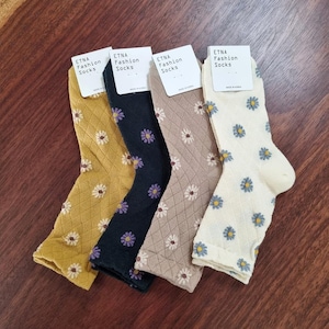 May include: Four pairs of socks with daisy patterns in mustard yellow, black, tan, and cream. Each pair has a tag that reads "ETNA Fashion Socks."
