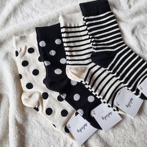 May include: Four pairs of socks with various patterns, including polka dots and stripes. The socks are black and white, with tags that say "melody". The socks are arranged on a white, textured surface.