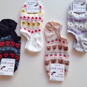 May include: Four pairs of low-cut ankle socks with various patterns including red hearts, yellow smiley faces, brown teddy bears, cherries, and white flowers. Each pair features a paper tag with Korean text and a graphic of a foot in a shoe.