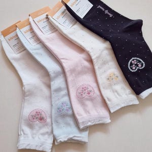 May include: A collection of five pairs of socks in various colors: white, light blue, pink, and black. Each sock features a heart-shaped floral embroidery and small polka dots. The socks have a tag that says "kikiyasocks".