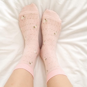May include: A pair of light pink socks with a floral pattern and a diamond-shaped openwork design. The socks have a solid pink cuff and toe. The socks are on a white surface.