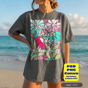 May include: A dark gray t-shirt with a floral design that says "Your Design Here" and "Mockup Ready". The shirt has short sleeves and a relaxed fit. The image also includes a yellow box with text that says "PSD PNG Canva Comfort Colors 1717" and "Pepper - C1717".