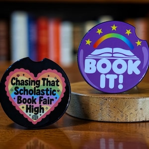 May include: A white ceramic mug with a black handle and the text "But First, Coffee" in a bold, black font. The mug is set against a blurred background, suggesting a cozy setting.