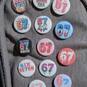 Peut inclure: Plusieurs badges ronds colorés avec le chiffre 67 et des motifs variés. On y trouve des fraises, des paillettes et des inscriptions telles que "Rizz Level" et "Six Seven".