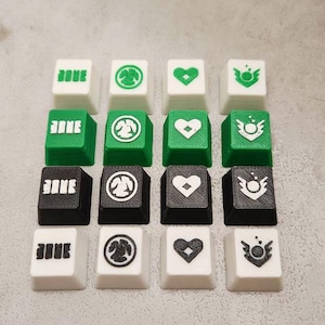 May include: A collection of sixteen custom keycaps in white, green, and black. Each keycap features a unique design, including text and various symbols. The keycaps are arranged in a grid pattern, offering a variety of colors and designs.